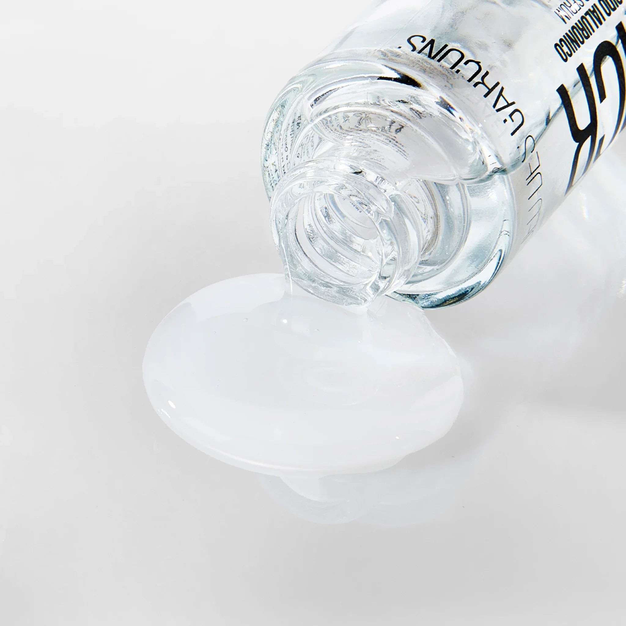 Siero trasparente all'acido ialuronico che fuoriesce da un flacone di vetro su sfondo bianco