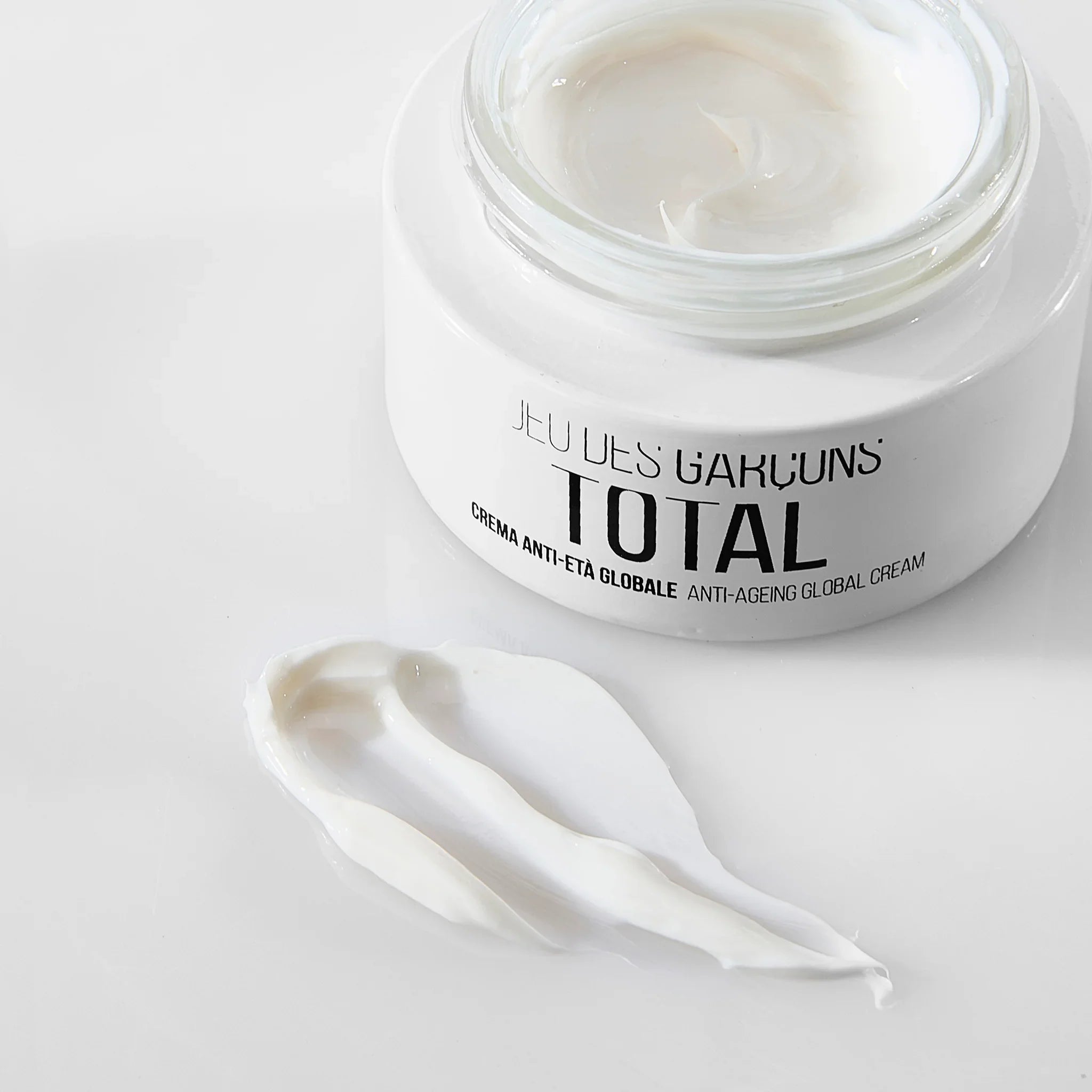 Barattolo di crema antietà globale Total con crema bianca spalmata su superficie bianca