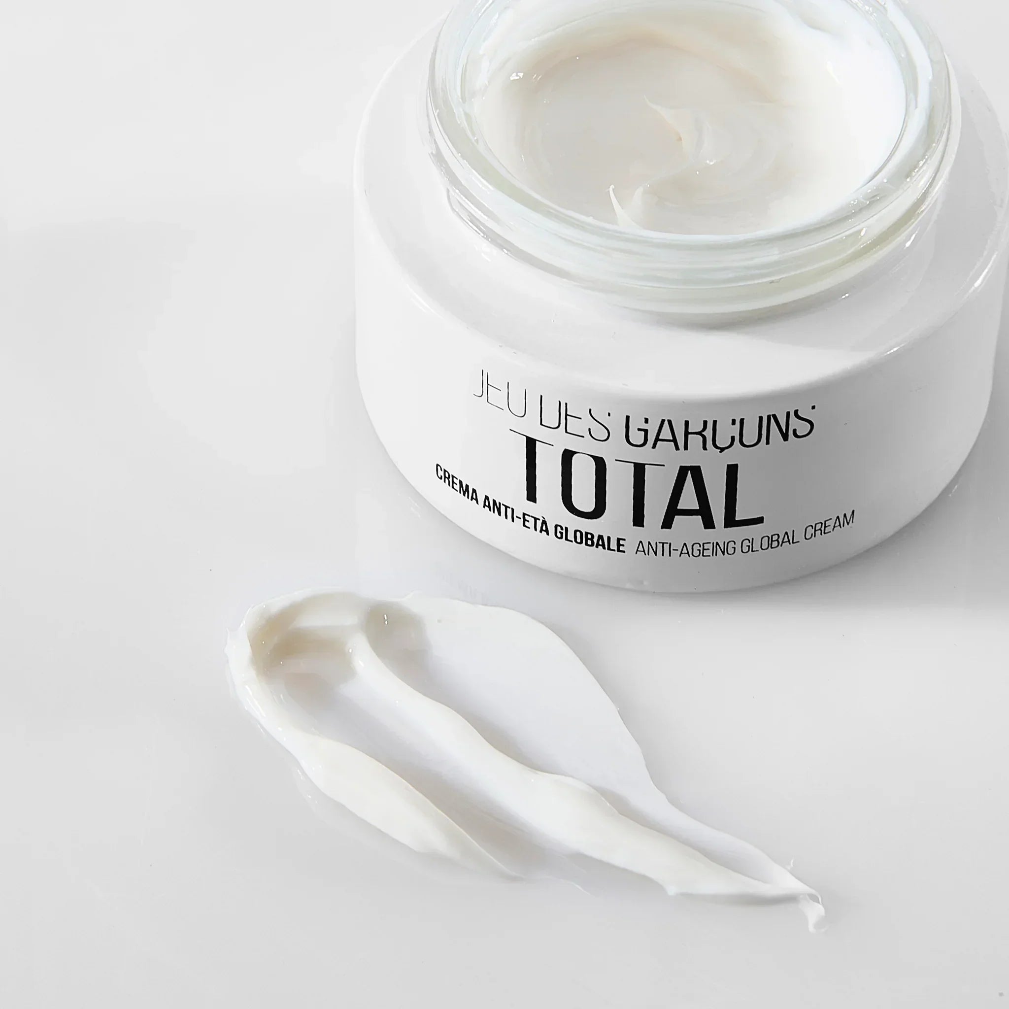 Barattolo di crema antietà globale Total con crema bianca spalmata su superficie bianca
