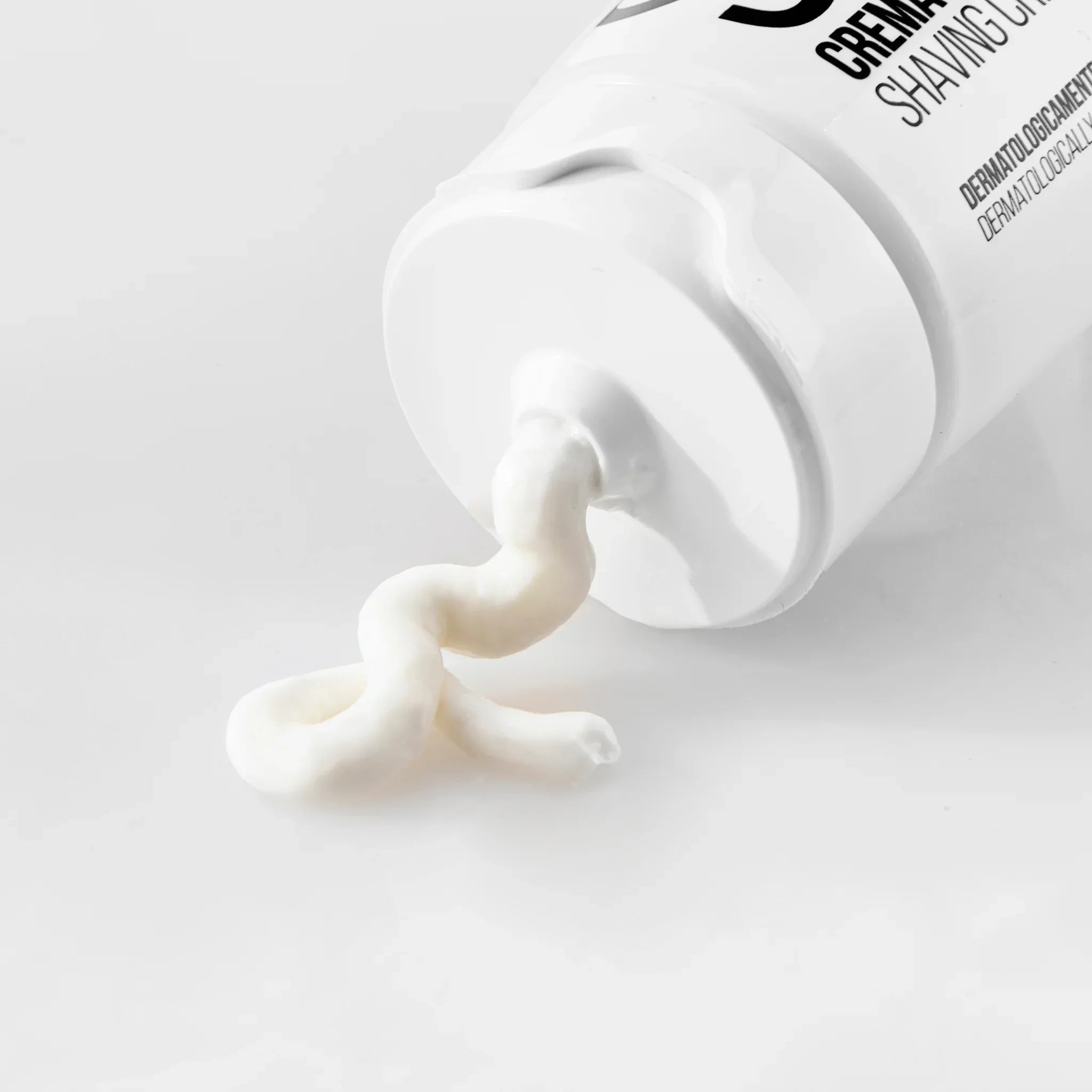 Crema da barba bianca spalmata fuori da un tubetto su fondo chiaro, crema uomo dermatologicamente testata