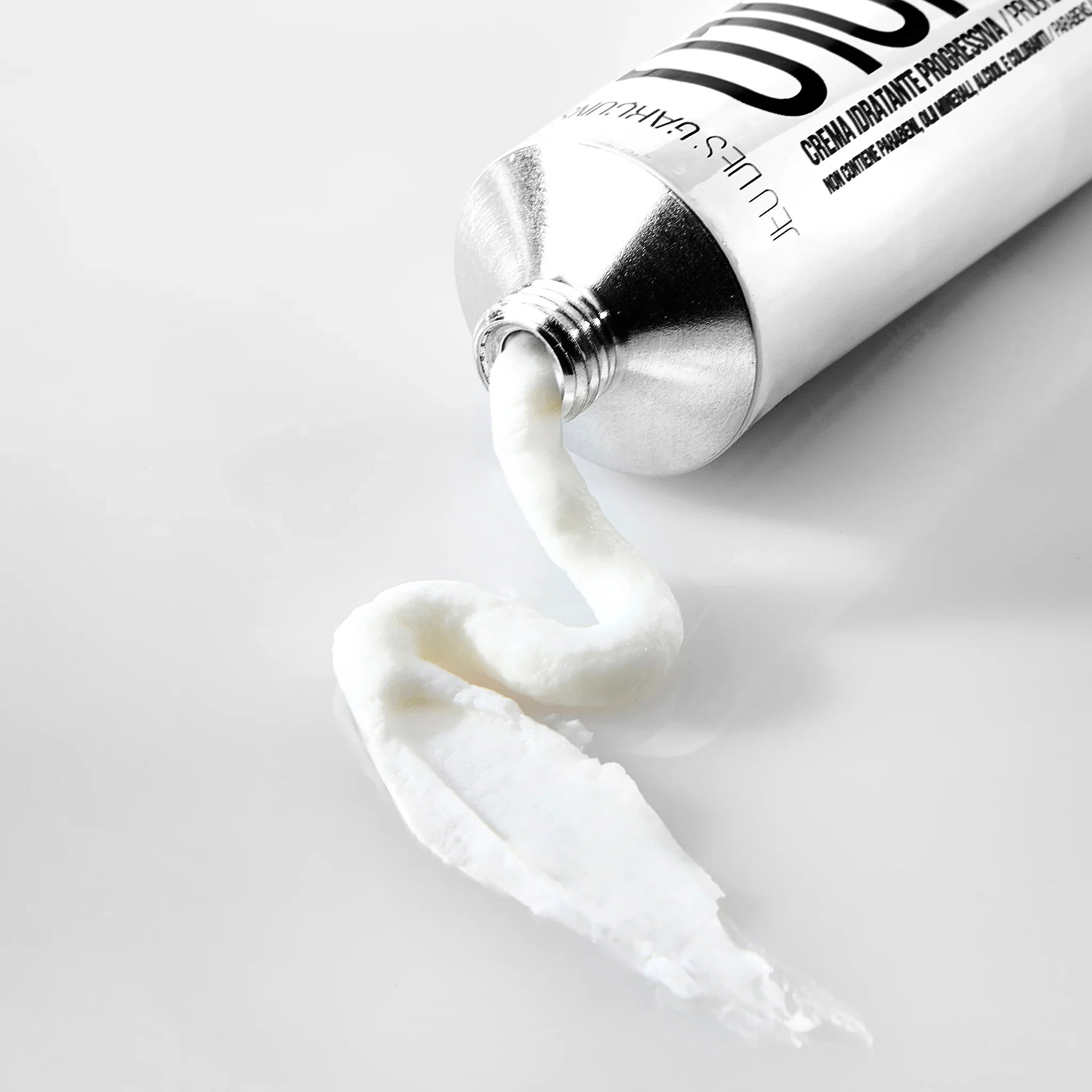 Crema viso idratante bianca estrusa da tubo metallico, texture densa e cremosa su sfondo bianco