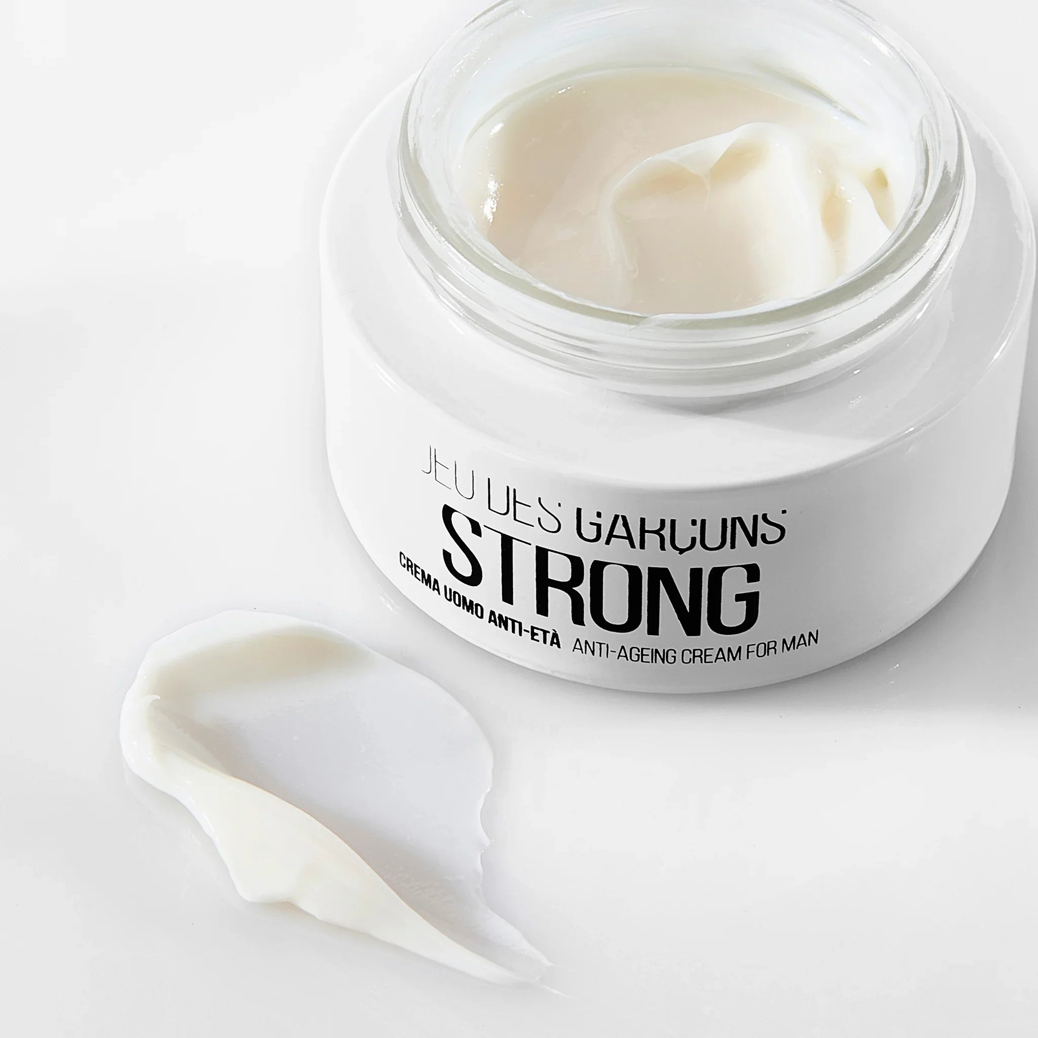 Barattolo di crema viso uomo anti-età Strong con texture cremosa bianca su sfondo bianco