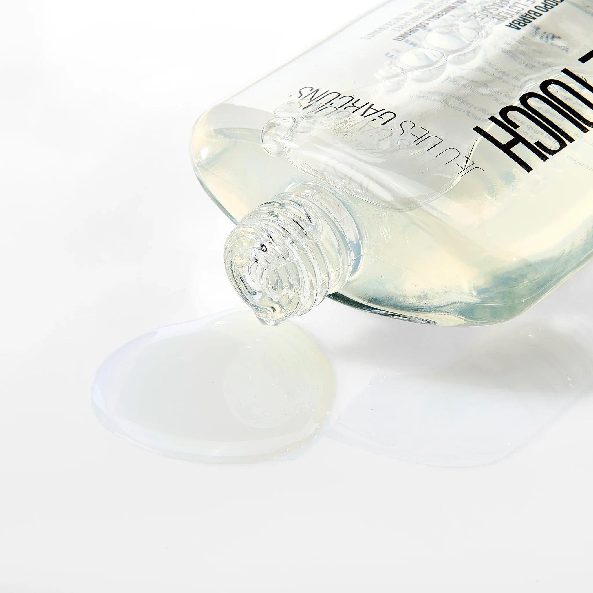 Bottiglia di dopobarba alcolico trasparente con liquido versato su superficie bianca