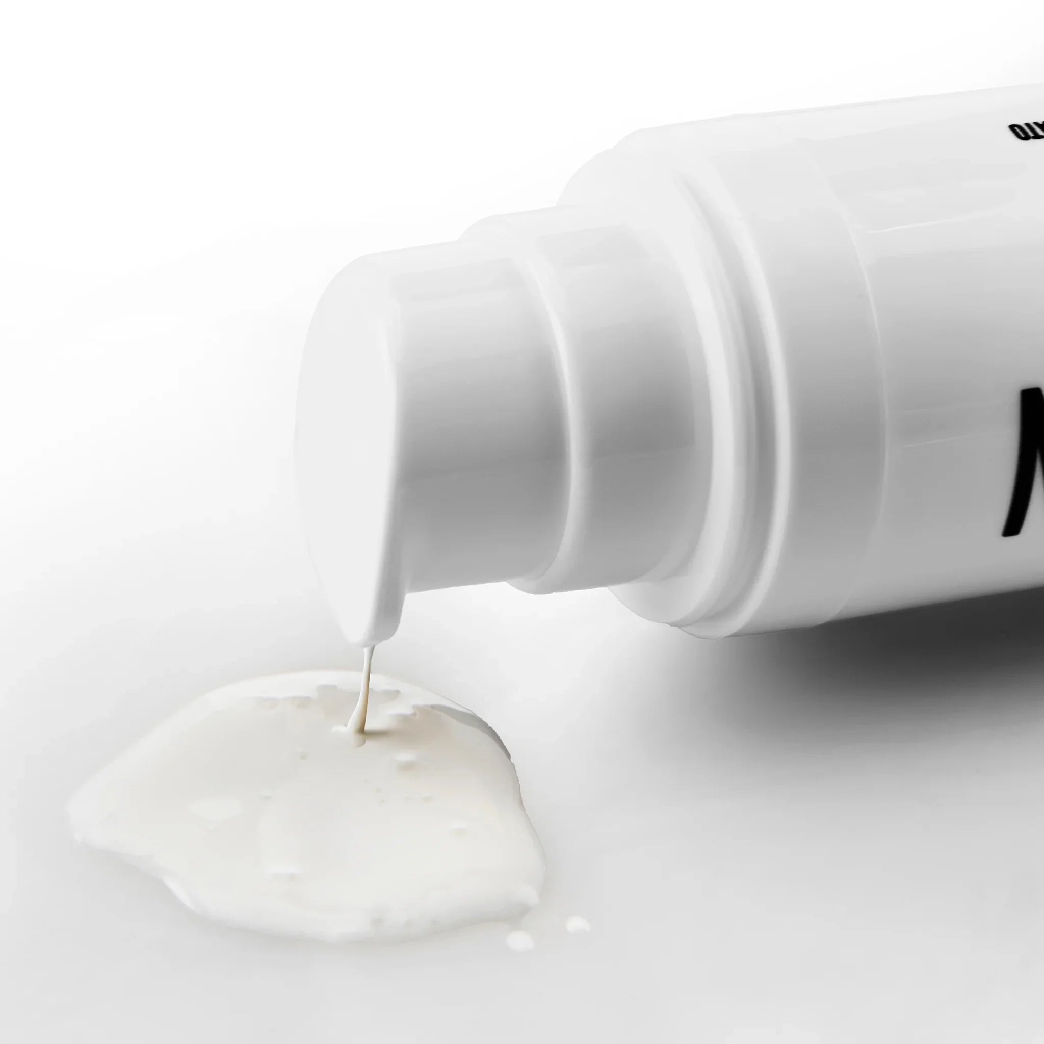 Dettaglio di flacone bianco con dispenser che eroga crema o lozione bianca su sfondo chiaro