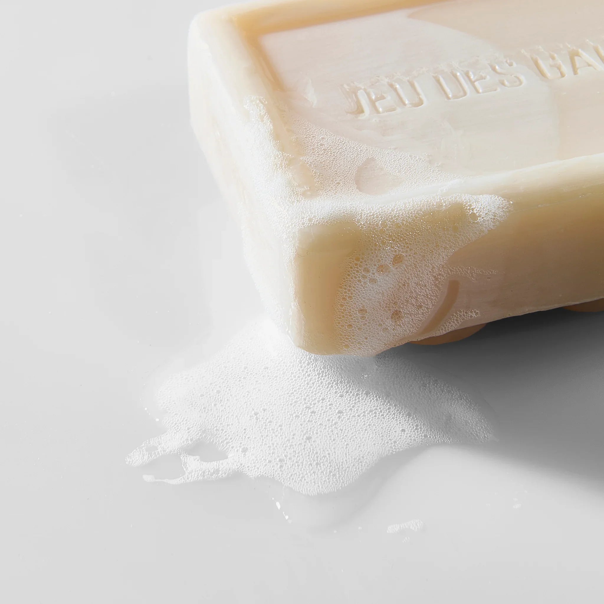 Sapone solido beige con schiuma bianca su superficie chiara, detergente naturale in uso